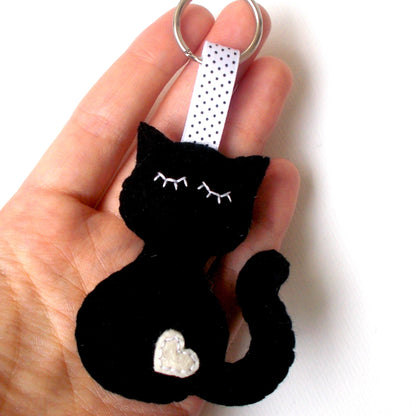 Black cat-shaped keychain with a white heart on a white background