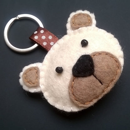 Felt keychain shaped like a bear face with a brown nose on a dark background
