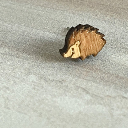 A tiny, handmade wooden hedgehog stud earring on a textured background.
